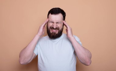 Mutsuz, üzgün bir adam şakaklarına masaj yapıyor. Bej arka planda stüdyoda korkunç bir acıyı dindirmeye çalışıyor..