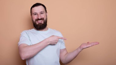 Yakışıklı, sakallı, kendine güvenen, bej arka planda boş kopya alanı gösteren bir adam.                    