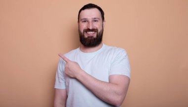 Yakışıklı, sakallı, kendine güvenen, bej arka planda boş kopya alanı gösteren bir adam.                    