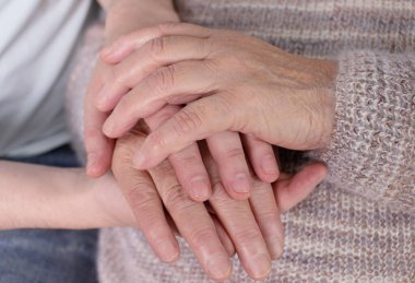 Yakın plan, yaşlı kadın, tanınmayan bir adamın elini tutuyor. Şefkatli bir büyükanne, torununu destekliyor. Kanepede yan yana oturuyor..