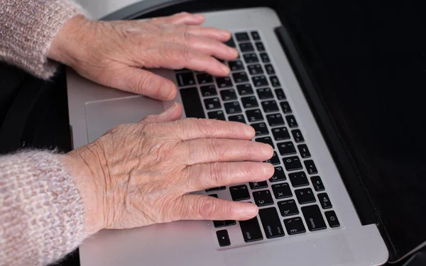 Close-up view of elderly woman using computer at home office. Remote work concept. Senior woman buy on-line, spend free time on internet, enjoy communication in social media, resting at home.