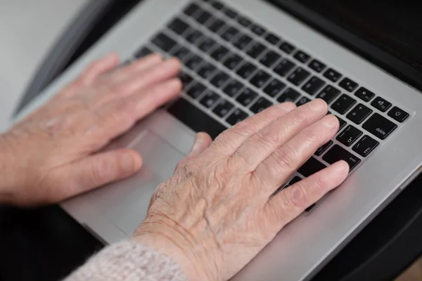 Close-up view of elderly woman using computer at home office. Remote work concept. Senior woman buy on-line, spend free time on internet, enjoy communication in social media, resting at home.