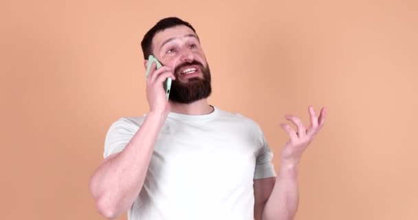 ベージュの背景で電話で話している若い男 — ストック動画