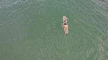 Okyanusta sörf tahtasında bir insan var. Su sakin ve gökyüzü berrak.