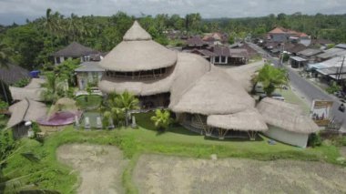 Bali, Endonezya - 14 Eylül 2022. Çatı sazdan yapılmış ve arka planda bir sürü ağaç olan büyük bir bina. Bina yemyeşil bir alanla çevrili.