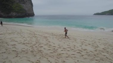 Arka planda okyanus olan bir adam sahilde koşuyor.