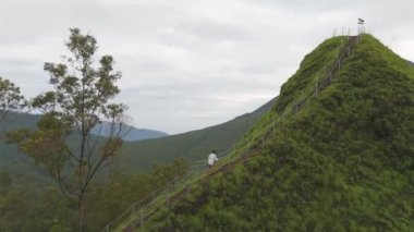 Flores, Endonezya 23 Aralık 2023. Arka planda yeşil bir ormanla dik bir tepede yürüyen bir insan. Sahne huzurlu ve huzurlu. Toprağın doğal güzelliğinin tadını çıkaran kişi.
