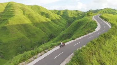 Sumba, Endonezya. Arka planda dağların güzel manzarası olan bir yolda motosiklet süren adamın hava manzarası..