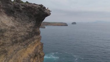 Lombok, Endonezya. Okyanusa bakan bir uçurumda oturan bir adam. Sahne sakin ve huzurlu, manzaranın ve dalgaların altında.           