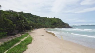 Sahilde kayalık bir kıyı şeridi ve kumsalda yürüyen birkaç kişi.