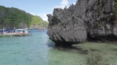 Uzaklarda yüzen tekneleri olan kayalık bir kıyı şeridi olan güzel mavi bir okyanus. Twin Lagoon, Coron, Palawan Filipinlerindeki Karst Kayalıkları.