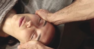 Masada yatan genç ve güzel bir kadının yüzüne masaj yapan adamın yakın plan görüntüsü.                        