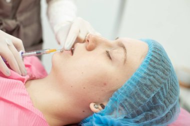 Modern güzellik salonunda gözleri kapalı yatan genç bir kadına gençleştirici iğne yapan profesyonel bir kadın. Enjeksiyonla pürüzsüz kırışıklık kavramı       