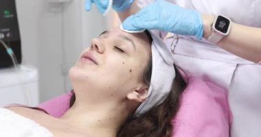 Güzellik salonunda kozmetik uzmanı tarafından yüz bakımı gören çekici bir genç kadın.         