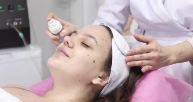 Güzellik salonunda kozmetik uzmanı tarafından yüz bakımı gören çekici bir genç kadın.         