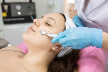 Güzellik salonunda kozmetik uzmanı tarafından yüz bakımı gören çekici bir genç kadın.         