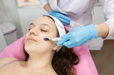 Güzellik salonunda kozmetik uzmanı tarafından yüz bakımı gören çekici bir genç kadın.         