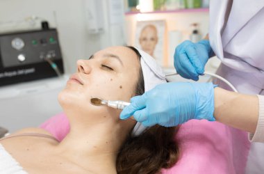 Güzellik salonunda kozmetik uzmanı tarafından yüz bakımı gören çekici bir genç kadın.         