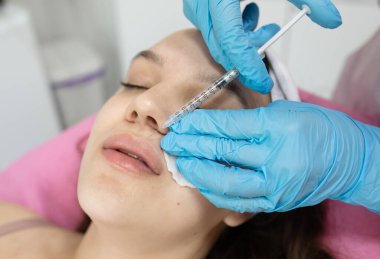 Güzel bir kadının kozmetoloji salonunda iğne olurken yakın çekimi. Şırınga enjekte eden dudakları olan tıp eldivenli doktor.                   