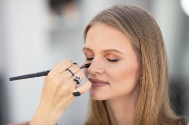 Genç profesyonel makyaj sanatçısı güzellik salonundaki güzel genç bayana kozmetik uyguluyor.    