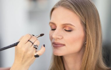 Genç profesyonel makyaj sanatçısı güzellik salonundaki güzel genç bayana kozmetik uyguluyor.    