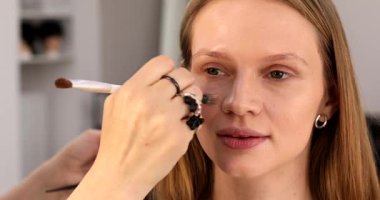 Profesyonel makyöz güzel genç bir kadınla çalışıyor. Makyaj sanatçısı cazibe modeline makyaj yapıyor             