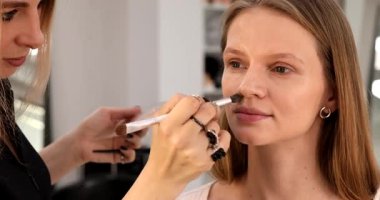 Profesyonel makyöz güzel genç bir kadınla çalışıyor. Makyaj sanatçısı cazibe modeline makyaj yapıyor             