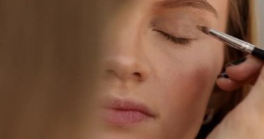 Stüdyoda makyajlı genç ve güzel bir kız. Makyöz güzellik salonuna göz farı sürüyor, yakın plan.                