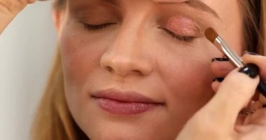 Stüdyoda makyajlı genç ve güzel bir kız. Makyöz güzellik salonuna göz farı sürüyor, yakın plan.                