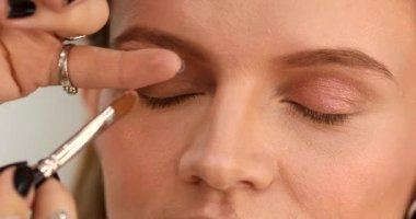 Stüdyoda makyajlı genç ve güzel bir kız. Makyöz güzellik salonuna göz farı sürüyor, yakın plan.                