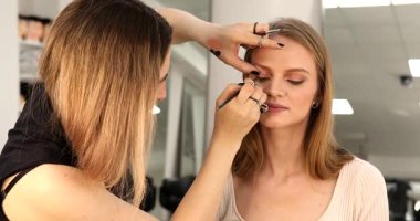 Makyöz güzellik stüdyosunda çalışıyor. Profesyonel makyaj ustası tarafından başvurulan kadın portresi.             