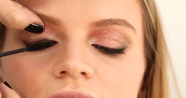 Makyöz, genç bir kadın için makyaj yapıyor, uzun kirpiklerine siyah rimel sürüyor. Profesyonel makyaj ve güzellik salonu konsepti.     