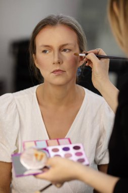 Makyöz, güzellik salonunda genç bir kadının profesyonel makyajını yapıyor.                              