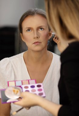 Makyöz, güzellik salonunda genç bir kadının profesyonel makyajını yapıyor.                              