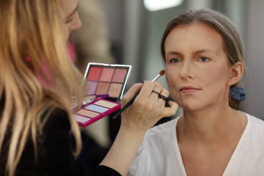 Makyöz, güzellik salonunda genç bir kadının profesyonel makyajını yapıyor.                              