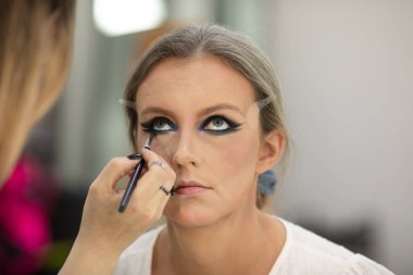 Güzellik salonunda genç bir bayanın makyajını yapan profesyonel makyözün yakın çekimi. Profesyonel göz makyajı modeli. 
