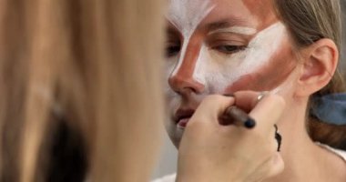 Makyaj sanatçısı genç ve güzel bir kadınla profesyonel makyaj yapıyor. Kadının yüzü bronzlaşmış ve beyaza boyanmış..      