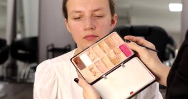 Makyaj sanatçısı genç ve güzel bir kadınla profesyonel makyaj yapıyor. Kadının yüzü bronzlaşmış ve beyaza boyanmış..      