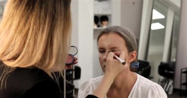 Makyöz, güzellik salonunda genç bir kadının profesyonel makyajını yapıyor.                              