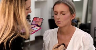 Makyaj sanatçısı güzellik salonundaki güzel genç bayana makyaj yapıyor.  