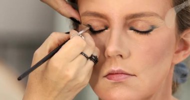 Güzellik salonunda genç bir bayanın makyajını yapan profesyonel makyözün yakın çekimi. Profesyonel göz makyajı modeli. Güzellik endüstrisi kozmetik, sahne arkasında profesyonel makyaj..                         