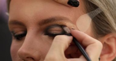 Güzellik salonunda genç bir bayanın makyajını yapan profesyonel makyözün yakın çekimi. Profesyonel göz makyajı modeli. Güzellik endüstrisi kozmetik, sahne arkasında profesyonel makyaj..                         