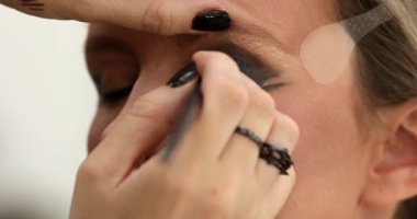 Güzellik salonunda genç bir bayanın makyajını yapan profesyonel makyözün yakın çekimi. Profesyonel göz makyajı modeli. Güzellik endüstrisi kozmetik, sahne arkasında profesyonel makyaj..                         