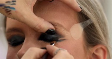 Güzellik salonunda genç bir bayanın makyajını yapan profesyonel makyözün yakın çekimi. Profesyonel göz makyajı modeli. Güzellik endüstrisi kozmetik, sahne arkasında profesyonel makyaj..                         