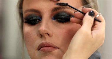 Güzellik salonunda genç bir bayanın makyajını yapan profesyonel makyözün yakın çekimi. Profesyonel göz makyajı modeli. Güzellik endüstrisi kozmetik, sahne arkasında profesyonel makyaj..                         