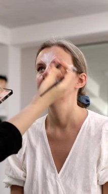 Makyöz, güzellik salonunda genç bir kadının profesyonel makyajını yapıyor.                              