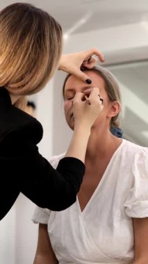 Makyöz, güzellik salonunda genç bir kadının profesyonel makyajını yapıyor.                              