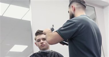 Erkek berber, berber dükkanında kırpıcıyla erkek müşterinin saçını kesiyor. Saç şekillendirme süreci.                