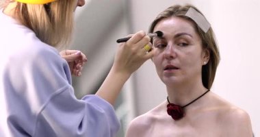 Makyöz, güzellik salonunda genç bir kadının profesyonel makyajını yapıyor.                