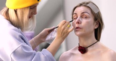 Makyöz, güzellik salonunda genç bir kadının profesyonel makyajını yapıyor.                